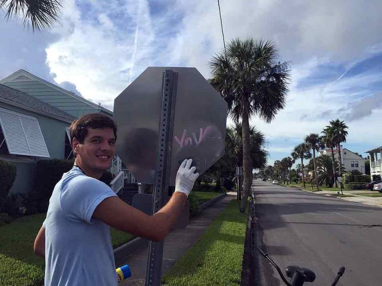man cleaning graffiti off a stop sign