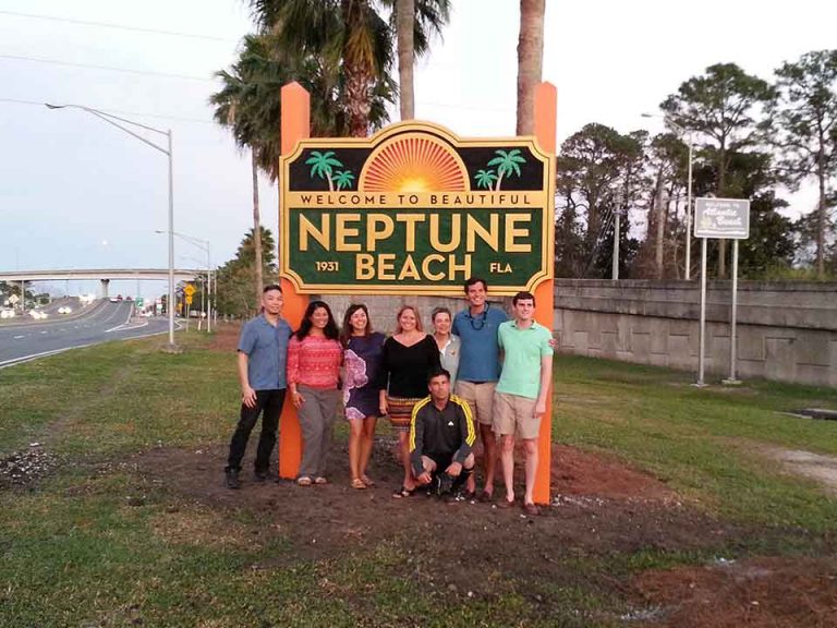 group of people standing in front of the Welcome to Neptune Beach sign near roadways